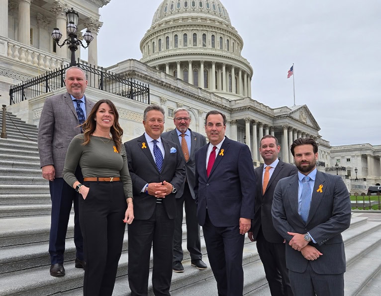 Group in professionals attire standing on steps outside of the U.S. Capitol building