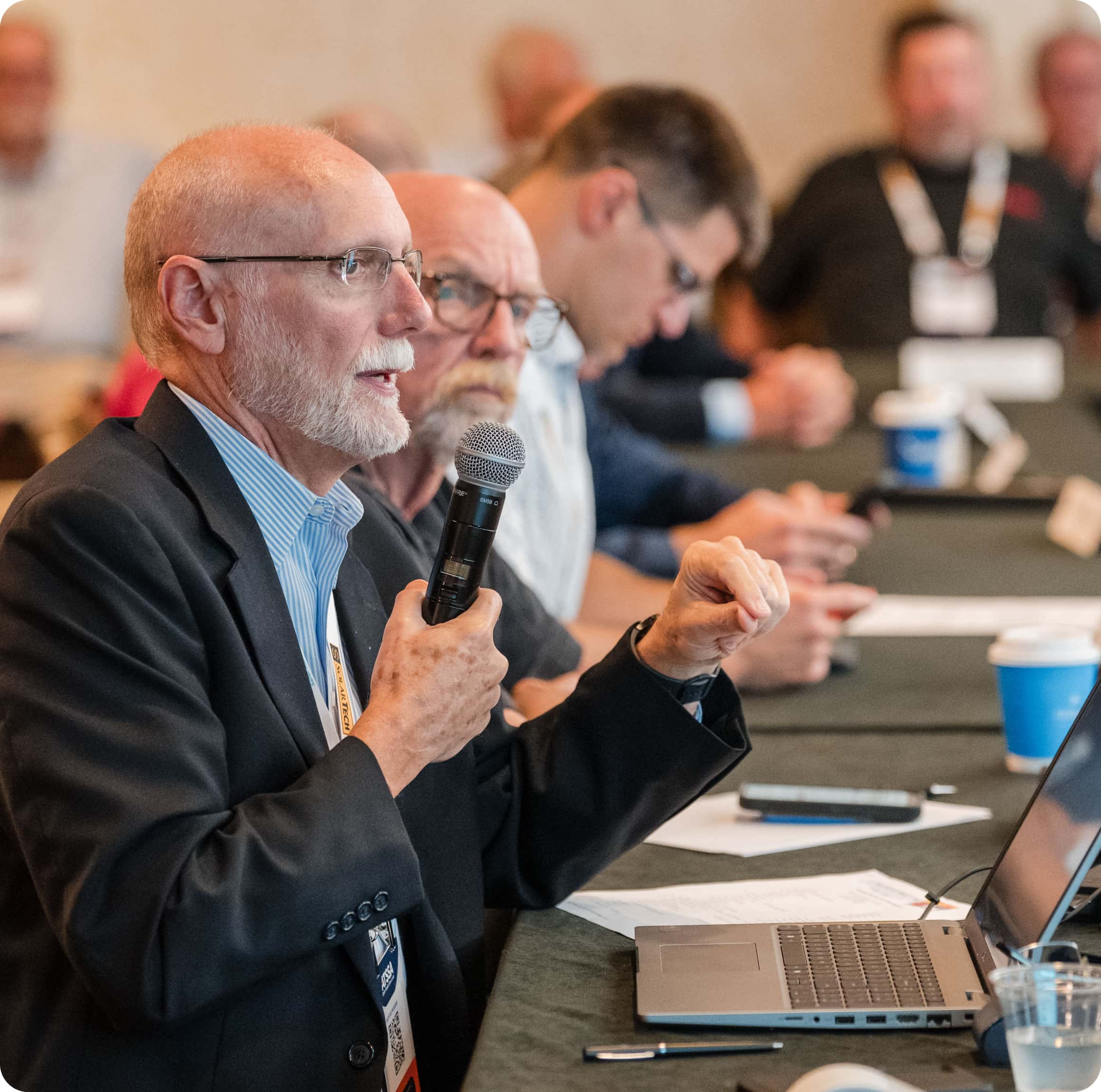 Adults sitting at a meeting table with a man holding a mic in the forefront