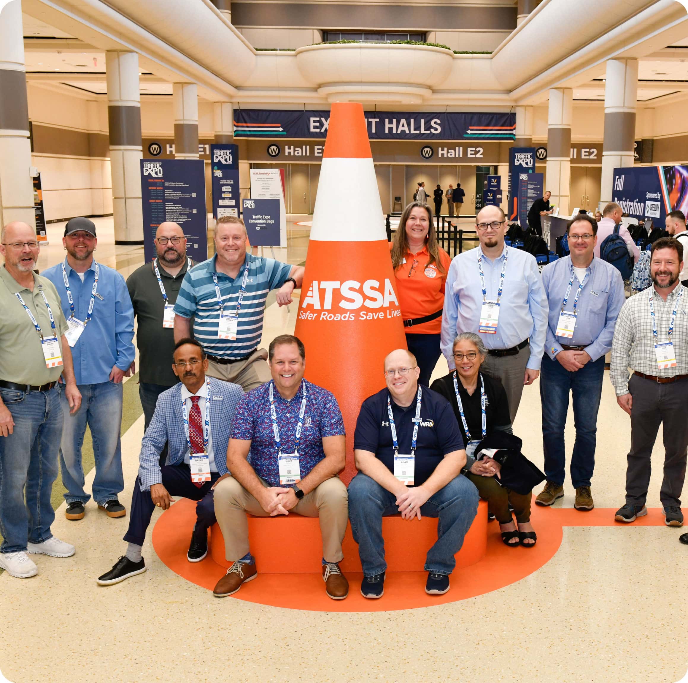 Group of men and women standing and sitting around an extra large traffic cone in a convention building